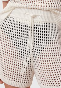 Hvide strikkede shorts med et løst netdesign, med en snørrebåndtalje og ribbede detaljer langs kanten for ekstra tekstur.