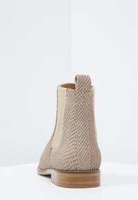 Beżowe botki sięgające kostki z plecioną teksturą, elastycznymi bocznymi panelami i niskim drewnianym obcasem. Gładkie wykończenie i miękki detal z boku.