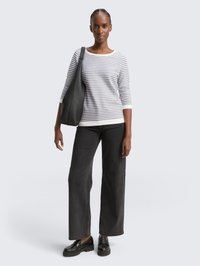 Suéter a rayas en gris y blanco con un escote amplio, combinado con unos vaqueros de pierna ancha negros, mocasines negros y un bolso negro de hombro.