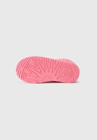 Semelle de chaussure en caoutchouc rose avec un motif de grip texturé, comportant des sillons et des rainures pour une traction optimale. Logo "UGG" en relief est visible.