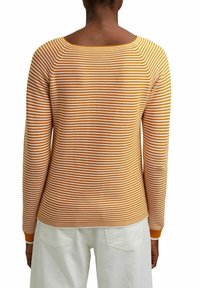 Gestreifter Pullover in Gelb und Weiß mit weitem Ausschnitt, langen Ärmeln und gerippten Bündchen. Weicher Strickstoff, über weißen Hosen getragen.