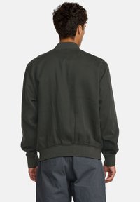 Giubbotto bomber verde oliva con polsini e orlo a coste, caratterizzato da una texture liscia e linee semplici e pulite. Vista dal retro.