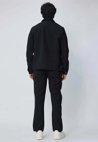 Veste noire et pantalon, en tissu uni. La veste a un col et une coupe droite, associée à un pantalon droit et des chaussures blanches.