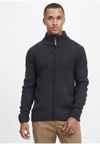 Mørkeblå strikket sweater med høj krave, struktureret overdel, lynlåslukning foran og farverige sprøjtninger i hele stoffet.