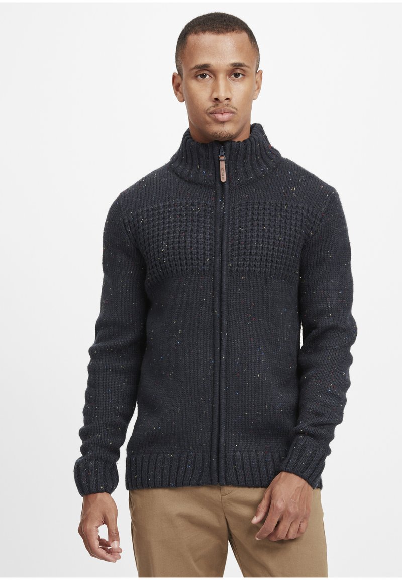 Mørkeblå strikket sweater med høj krave, struktureret overdel, lynlåslukning foran og farverige sprøjtninger i hele stoffet.