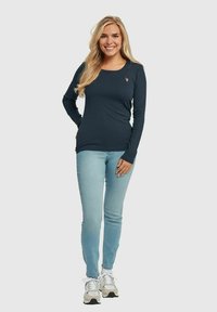Langermet marineblå ribbet skjorte med rund hals, kombinert med lyseblå jeans og hvite sneakers med grå detaljer.