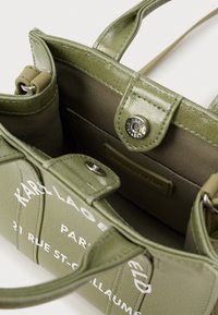 Olive green Karl Lagerfeld handbag with white text, open top showing snap button closure and inner pocket with brand label.