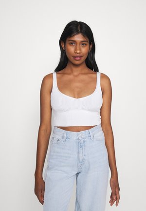 Top cropped branco com textura canelada, decote redondo e alças largas, combinado com jeans de denim de cintura alta em lavagem clara.