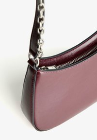 Burgundy nahkalaukku sileällä pinnalla, hopeaketjuolkaimella ja mustilla vetoketjuyksityiskohdilla, jossa on särmä muoto.