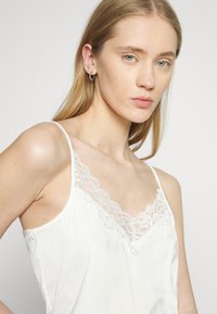 Witte camisole met een delicate kantafwerking bij de halslijn, dunne verstelbare bandjes en een zachte, gladde textuur.