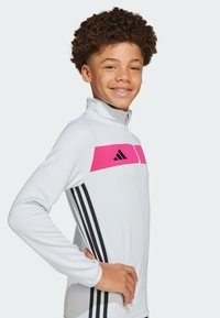 Witte zip-up sporttop met een brede roze streep en zwart Adidas-logo, met zwarte verticale strepen langs de mouwen.