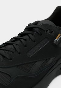 Sapatilha Reebok preta com atacadores pretos e etiqueta de tecido Cordura na lateral, exibindo costura detalhada e material texturizado.