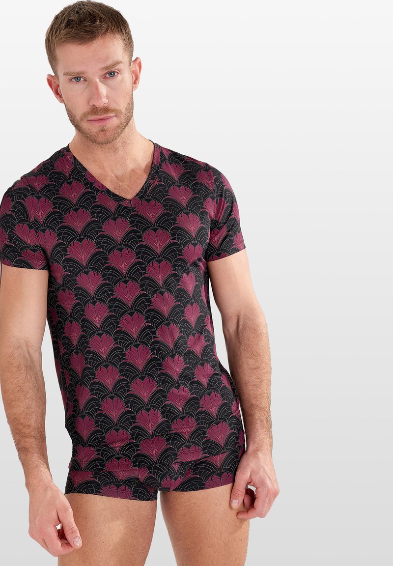 T-shirt noir à col en V avec un motif floral rose répétitif et des lignes courbes, à manches courtes et au design ajusté. Texture douce.