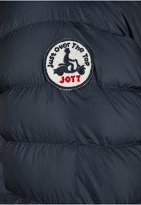 Giubbotto piumino blu navy con un'applicazione ricamata circolare che presenta un logo di uno scooter e la scritta "Just Over The Top" e "JOTT" in rosso.