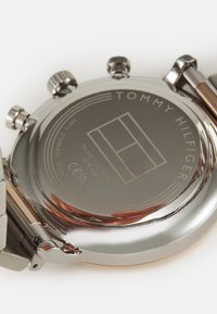 Fondo de reloj de acero inoxidable con logotipo y marcas grabadas. Cuenta con dos botones de presión y una superficie pulida. Resistente al agua hasta 5 bares.