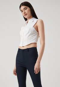 Hvit avkortet skjorte med krage, frontglidelås og sømdetaljer, parret med marineblå slim-fit bukser med flat front.