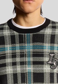Strickpullover mit einem schwarz-grau-blauen Karomuster, kurzem schwarzen Kragen und einem eingestickten "LS"-Detail auf der Brust.