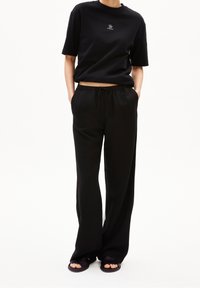Svart t-shirt med kort ärm och en liten logotyp, i kombination med löst sittande svarta byxor och mörka halksandaler med elastisk midja.