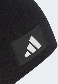 Zwarte beanie met een gestructureerd oppervlak, voorzien van een rechthoekig zwart label en een wit Adidas-logo ontwerp.