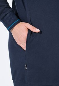 Felpa blu navy con polsini a coste testurizzati, dotata di una tasca laterale e di un piccolo tag nero con logo vicino all'orlo.