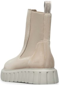 Beige ankelsko med elastiska sidor, mjuk mocka-textur och kraftig vit sula med horisontella spår. Dragflik bak.