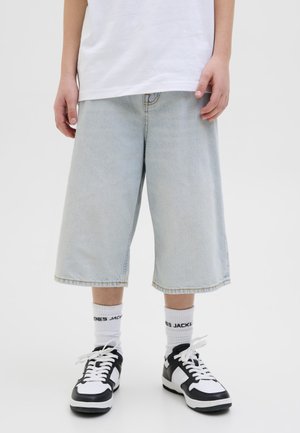 Person wearing light blue denim long shorts, white socks with black text, black and white sneakers, and a plain white T-shirt.