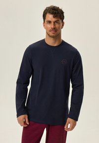 Granatowa koszula z długim rękawem i okrągłym dekoltem, z małym haftowanym logo w kolorze bordowym na piersi oraz miękkim, strukturalnym materiałem.