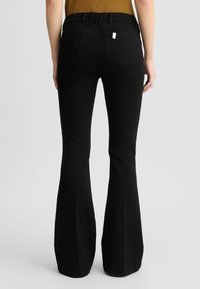 Zwarte flare jeans met een rekbare tailleband, twee achterzakken en subtiele stiksels. Smalle textuur en aansluitende pasvorm.