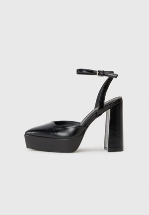 Black platform heels with a pointed toe and adjustable ankle strap. Constructed from smooth leather, featuring a chunky block heel.