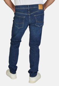 Jeans de mezclilla en azul oscuro con un ajuste Slim, que cuentan con una etiqueta de cuero en la parte posterior, dos bolsillos traseros y acentos de costura visibles.