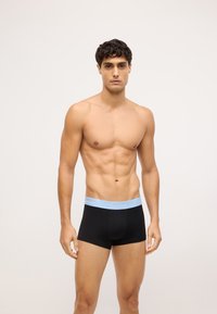 Čierne boxerky s bledomodrým pásom, na ktorom je logo 'Calvin Klein'. Tkanina vyzerá hladko, má priliehavý dizajn a elegantný tvar.