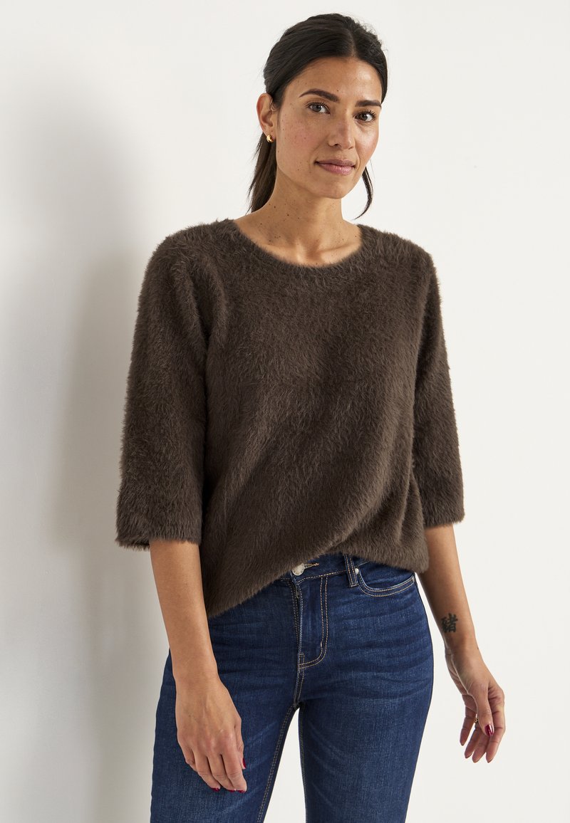 Bruine, fluffy gebreide trui met driekwart mouwen en een ronde hals, gecombineerd met donkerblauwe jeans. Zachte textuur, casual pasvorm.