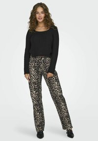 Musthave mustriba pikkade käistega lühike kampsun, mis on kombineeritud beežide leopardiliste pükstega. Pükstel on vabalt langev lõige, nööbiga sulgemine ja eristatav loomade muster.
