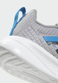 Gray athletic shoe featuring a textured upper with blue accents, a white sole, and a rubberized heel for grip and support.