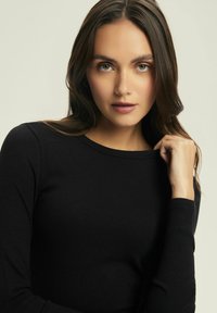 Czarny, prążkowany longsleeve z okrągłym dekoltem. Posiada dopasowane rękawy i teksturowany materiał. Minimalistyczny design bez widocznych wzorów.