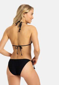 Bikini nero con un motivo testurizzato. Collo all'americana con spalline regolabili. Parte inferiore con lacci laterali regolabili. Design semplice ed elegante.