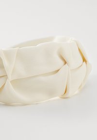 Knytt hvitt tøyhodebånd med teksturert overflate, som har et mykt, elastisk materiale og en glatt, rund form.