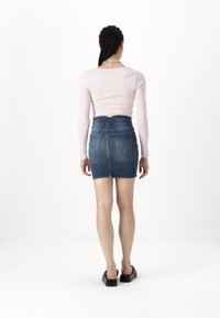Denim mini skjørt med en tettsittende midje og en subtil bakventil. Lys blå farge med to baklommer. Brukt sammen med en langermet rosa topp.
