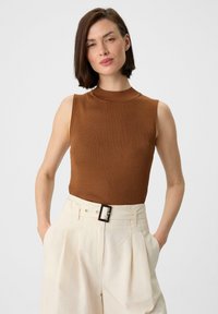Bruine mouwloze ribtop met hoge hals, gecombineerd met crème hoge taille geplooide broek met een zwart riemgesp detail.