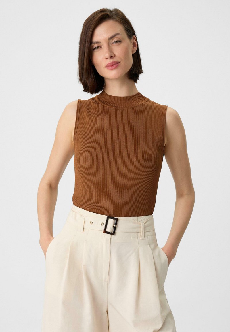 Bruine mouwloze ribtop met hoge hals, gecombineerd met crème hoge taille geplooide broek met een zwart riemgesp detail.