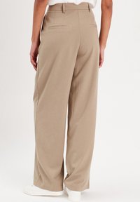 Pantalon large beige en tissu lisse, avec deux poches arrière et une taille haute. Associé à des baskets blanches.