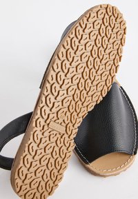 Sandale en cuir noir avec bout ouvert, semelle en caoutchouc texturée couleur tabac présentant un motif de bande hexagonal et taille 40 marquée "Made in Spain."