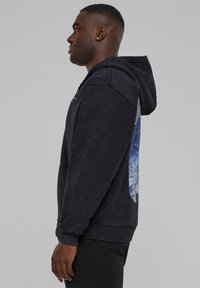 Mørkeblå hoodie med en kengurulomme, prydet med et stort grafisk tryk i blå og hvid på ryggen, lavet af blødt, tekstureret stof.
