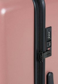 Valigia rigida rosa con superficie texturizzata, zip nera e lucchetto a combinazione sul lato. Design compatto e rettangolare.