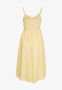 Žluté pruhované šaty se špagetovými ramínky a smockovaným trupem. Volná sukně dosahuje do poloviny l�ýtek a má lehkou texturu látky.