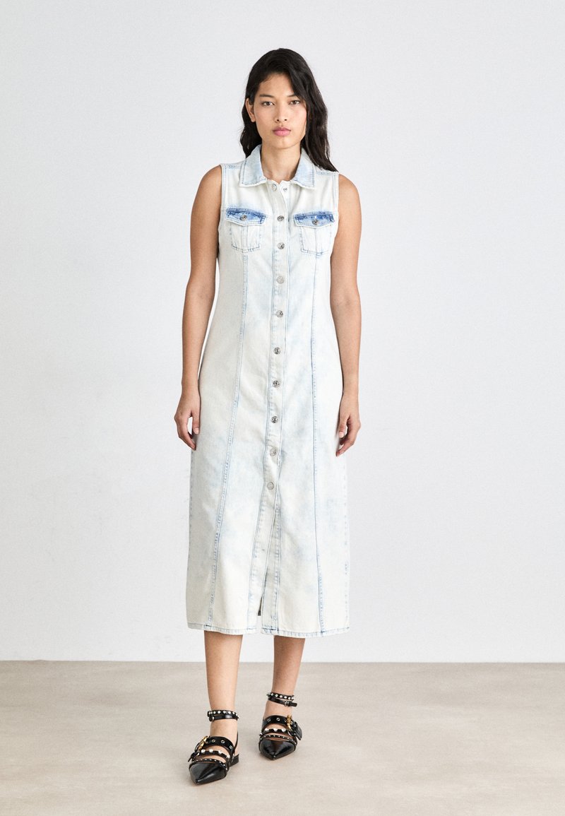 Ljusblå denimklänning utan ärmar med knappar framtill, två bröstfickor och en figurnära silhuett. Svarta spetsiga skor med nitar.