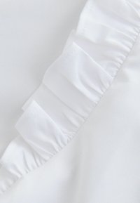 Tessuto bianco con una consistenza morbida, caratterizzato da un dettaglio arricciato lungo un bordo, creando un elemento di design delicato e stratificato.