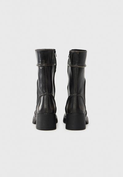 Μαύρες δερμάτινες μπότες μέσης μασχάλης με λεία υφή, ορθογώνιο τακούνι και φερμουάρ στο πλάι, με αντίθετες ραφές λεπτομερειών.