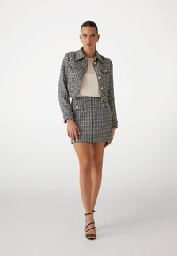 Set de sacou și fustă din tweed, alb-negru, cu nasturi aurii, având un design scurt și margini descoase. Asortat cu sandale negre cu curea.