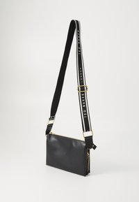 Borsa a tracolla nera in pelle con zip dorata, dotata di una tracolla regolabile a strisce con il testo "TED BAKER LONDON" e dettaglio a catena.